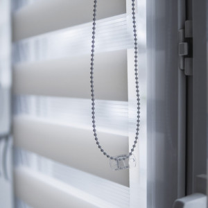 Details of white fabric roller blinds on the white plastic window in the living room. Close up on roll curtains indoor